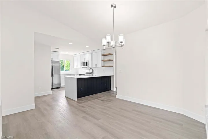 Kitchen with white cabinetry, light hardwood / wood-style floors, stainless steel appliances, kitchen peninsula, and decorative light fixtures