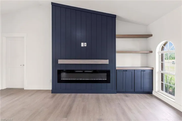 Unfurnished living room featuring a fireplace, light wood-type flooring, and vaulted ceiling