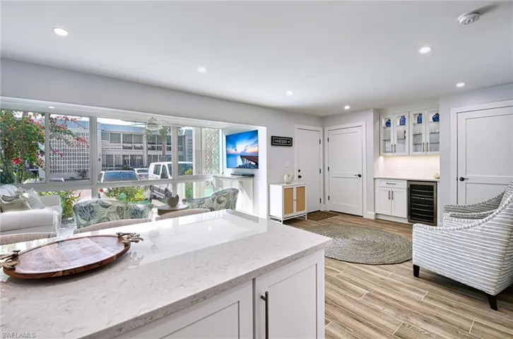 Kitchen featuring light hardwood / wood-style floors, beverage cooler, tasteful backsplash, light stone countertops, and white cabinets