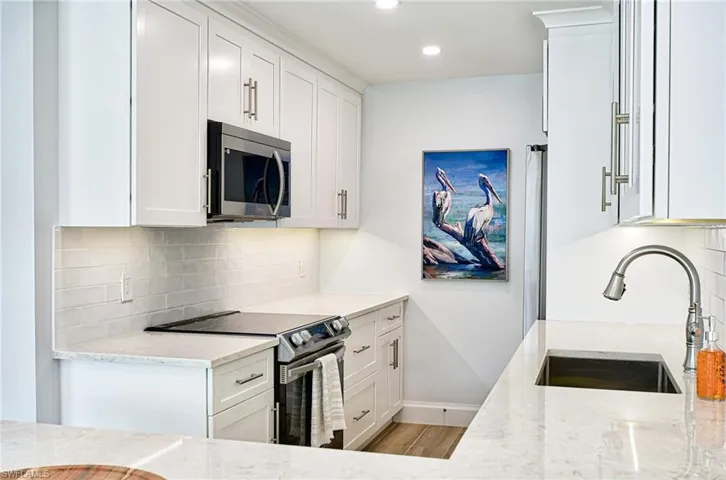Kitchen featuring electric stove, light wood-type flooring, backsplash, sink, and white cabinets