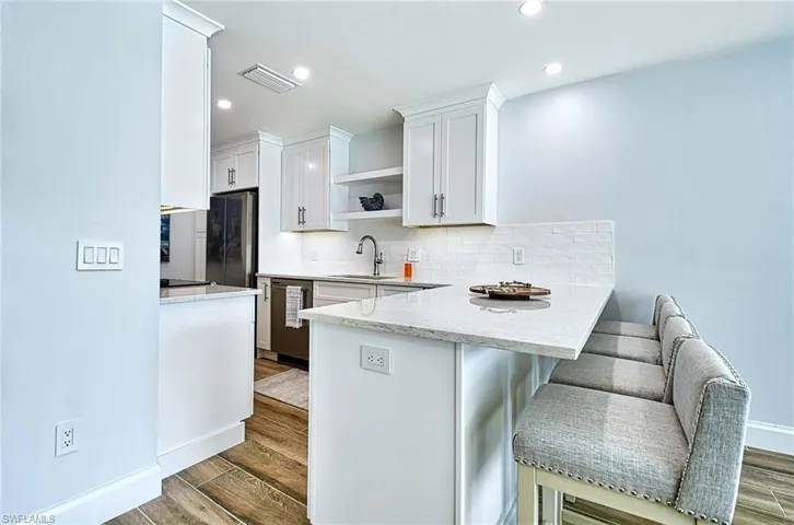 Kitchen featuring white cabinetry, kitchen peninsula, hardwood / wood-style floors, backsplash, and sink