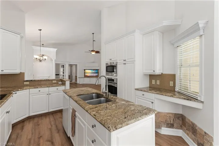 The kitchen features granite counters, a stainless steel sink, luxury vinyl flooring, white cabinets, goose-neck faucet, stainless steel appliances including a wall oven and microwave.