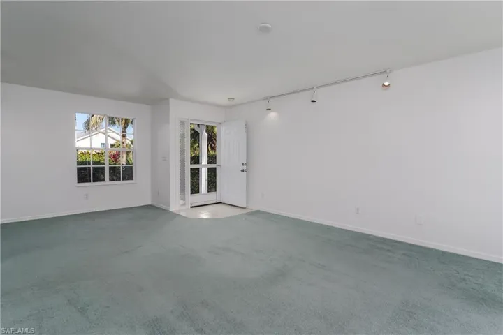 Carpeted empty room featuring track lighting and baseboards