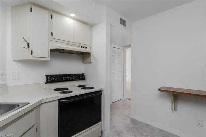 Kitchen featuring electric range oven, light countertops, and white cabinets
