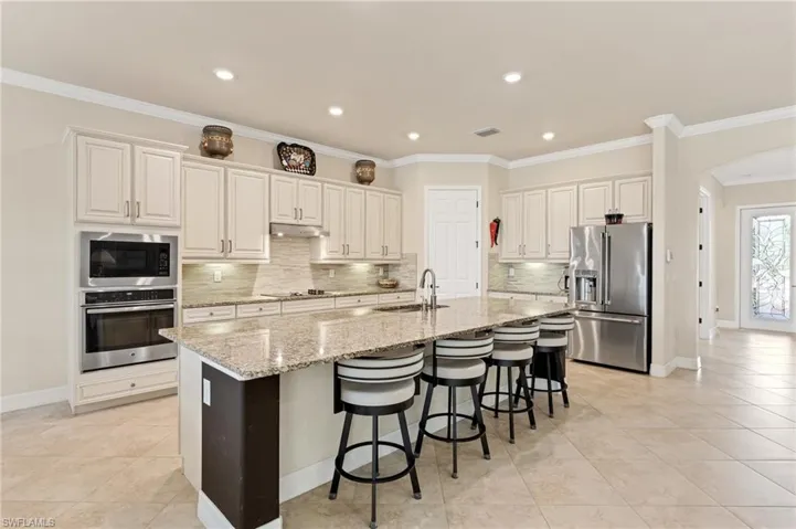 Kitchen featuring visible vents, arched walkways, appliances with stainless steel finishes, under cabinet range hood, and a sink