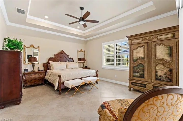 Bedroom featuring a tray ceiling, visible vents, crown molding, and baseboards