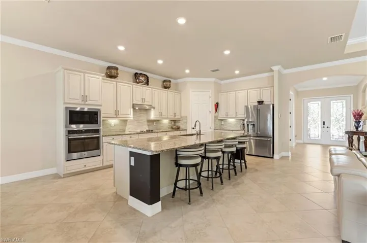 Kitchen featuring a center island with sink, arched walkways, light stone countertops, stainless steel appliances, and a kitchen bar