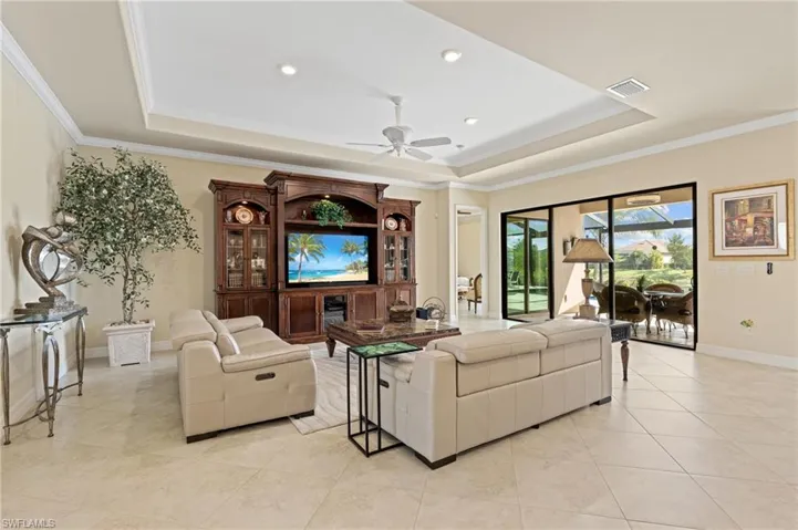 Living room with baseboards, visible vents, a raised ceiling, ornamental molding, and light tile patterned flooring