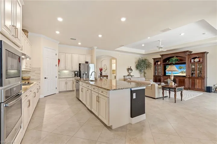 Kitchen with arched walkways, light stone counters, a kitchen island with sink, stainless steel appliances, and ornamental molding