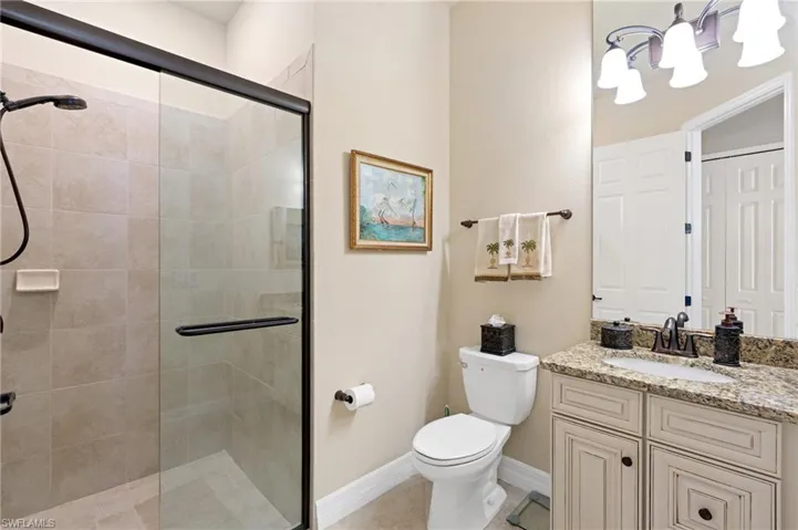 Bathroom featuring toilet, a notable chandelier, vanity, baseboards, and a stall shower