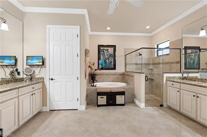 Full bathroom featuring crown molding, two vanities, a shower stall, tile patterned flooring, and a bath