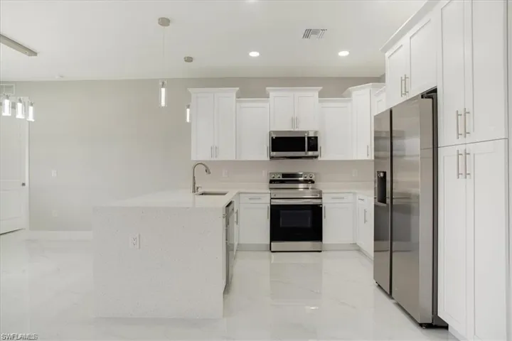 Kitchen with sink, stainless steel appliances, white cabinets, and hanging light fixtures