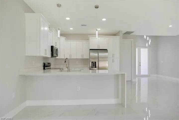 Kitchen featuring appliances with stainless steel finishes, sink, decorative light fixtures, and white cabinets