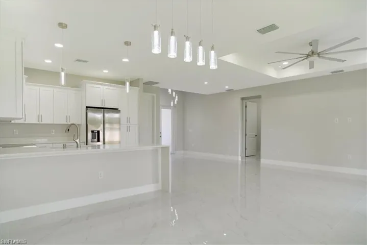 Kitchen with a kitchen island with sink, decorative light fixtures, ceiling fan, stainless steel fridge with ice dispenser, and white cabinets