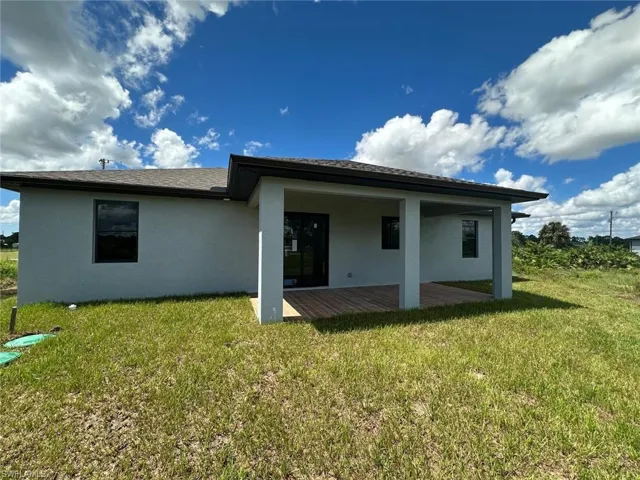 Back of house with stucco siding and a lawn