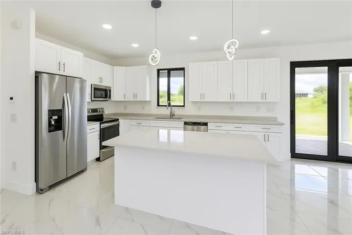 Kitchen with appliances with stainless steel finishes, decorative light fixtures, white cabinetry, light stone countertops, and a center island