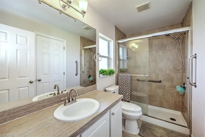 Full Jack and Jill bathroom featuring toilet, a shower stall, visible vents, and vanity.