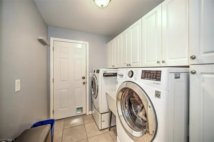 Utility Laundry area featuring washing machine and dryer with sink in between, tons of cabinet space, and light tile floors.