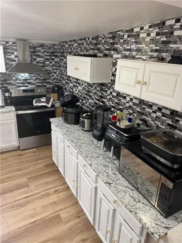 Kitchen featuring wood-finish flooring, white cabinetry with gold-tone hardware, granite-look countertops, and a full-height mosaic tile backsplash