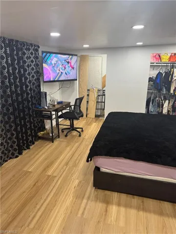 Room featuring wood-finish flooring throughout, recessed ceiling lighting, and a built-in open closet with shelving and hanging storage