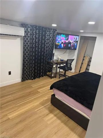 Room featuring wood-finish flooring, recessed ceiling lighting, and a wall-mounted air conditioning unit