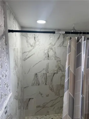 Shower featuring large-format tile walls with a marble-effect pattern, recessed ceiling lighting, and mosaic tile accents