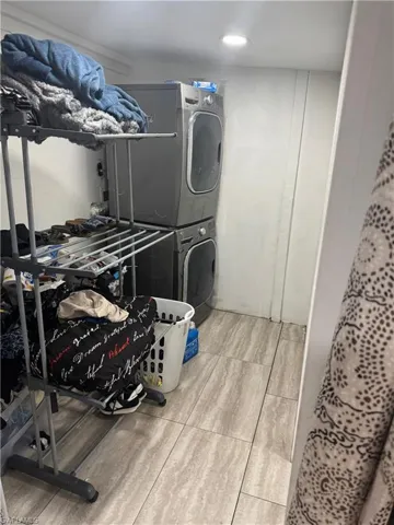 Laundry area featuring a stacked washer and dryer, recessed ceiling lighting, and light-toned tile flooring