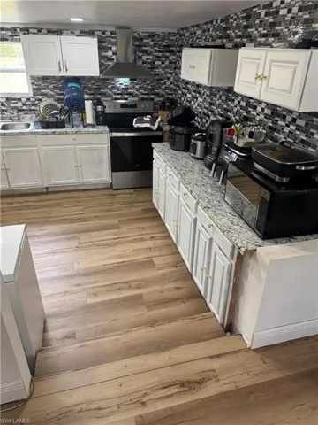 Well-appointed kitchen featuring wood-finish flooring, white cabinetry, granite-look countertops, a stainless steel range, and a mosaic tile backsplash
