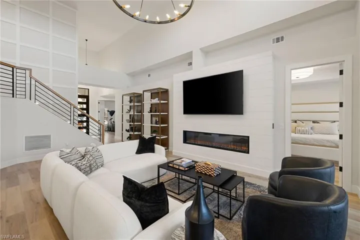 Living room with wood finished floors, a glass covered fireplace, stairs, a towering ceiling, and a chandelier