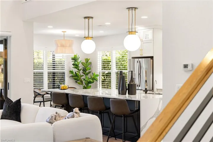 Kitchen with light stone countertops, white cabinetry, decorative light fixtures, a kitchen bar, and recessed lighting