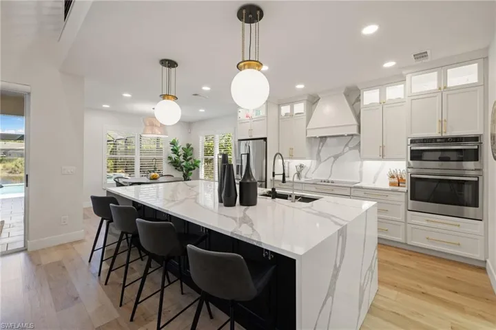 Kitchen featuring decorative light fixtures, glass insert cabinets, light stone countertops, white cabinetry, and recessed lighting