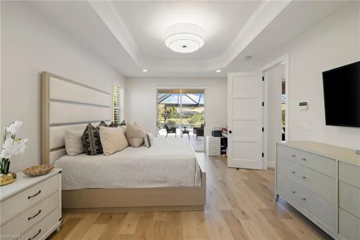 Bedroom featuring crown molding, light wood finished floors, access to outside, a tray ceiling, and recessed lighting