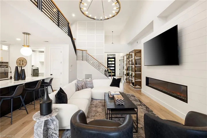 Living area with built in features, a glass covered fireplace, light wood finished floors, a chandelier, and stairway