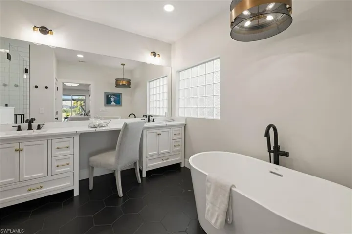 Bathroom featuring dark tile patterned flooring, two vanities, a soaking tub, and recessed lighting