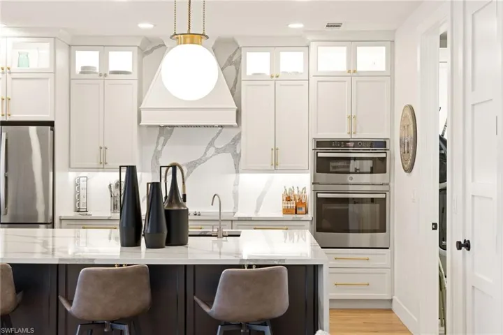 Kitchen featuring light stone countertops, appliances with stainless steel finishes, white cabinetry, a kitchen bar, and custom exhaust hood