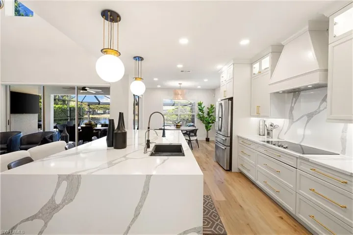 Kitchen with light stone counters, decorative light fixtures, premium range hood, recessed lighting, and white cabinets