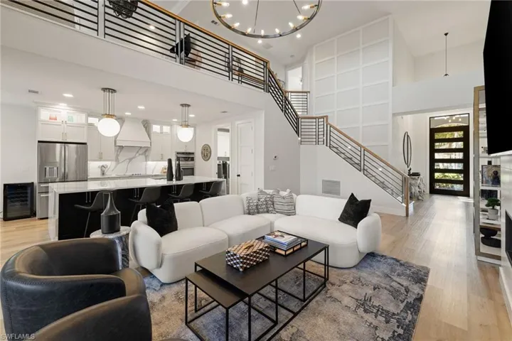 Living area featuring stairway, light wood-style floors, a towering ceiling, a chandelier, and wine cooler
