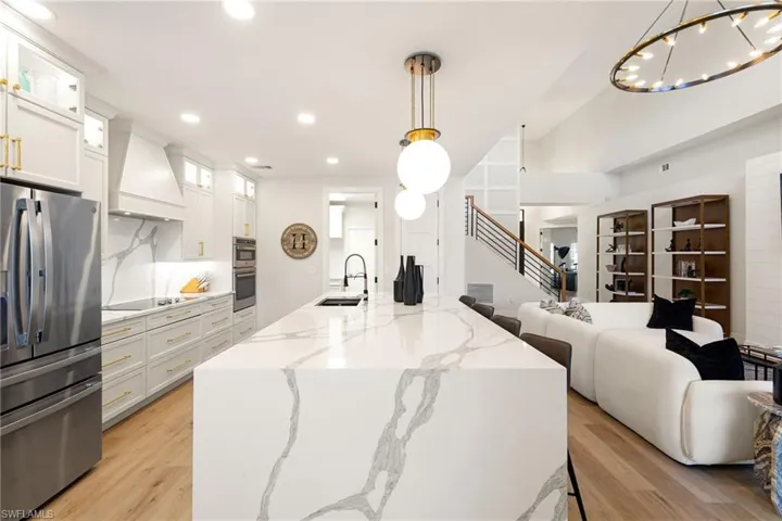 Kitchen featuring stainless steel appliances, glass insert cabinets, light stone counters, white cabinets, and pendant lighting