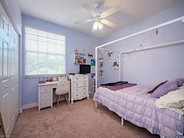 Carpeted bedroom featuring an office area, ceiling fan, and a closet