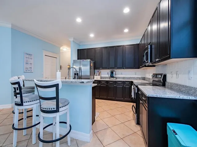 Kitchen with appliances with stainless steel finishes, a breakfast bar, light tile patterned floors, ornamental molding, and an island with sink