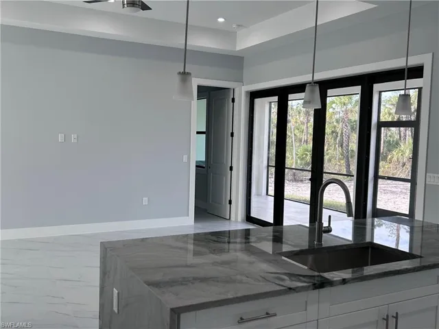 Kitchen with white cabinetry, french doors, sink, hanging light fixtures, and dark stone counters