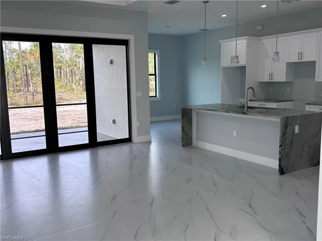 Kitchen with sink, light stone counters, backsplash, decorative light fixtures, and white cabinets