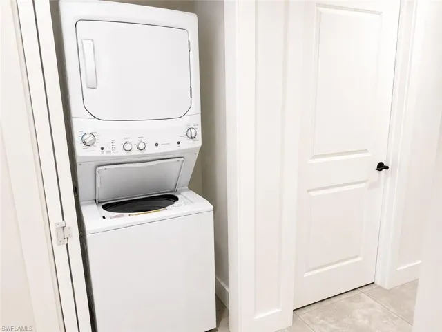 White stackable washer and dryer unit, white paneled doors with black hardware, and light-toned floor tiling