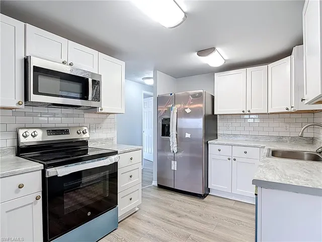 Kitchen with stainless steel appliances, white cabinets, light countertops, and tasteful backsplash