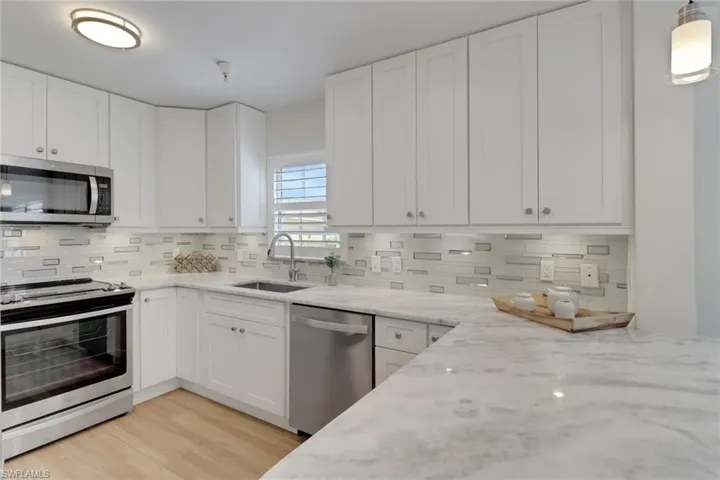Kitchen with white cabinets, stainless steel appliances, and light stone counters