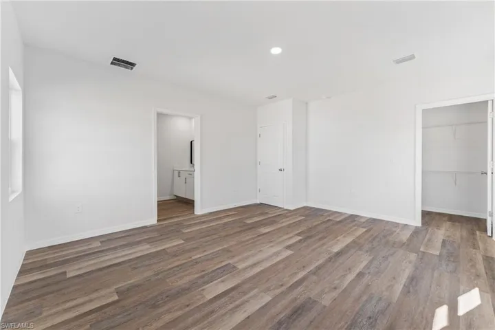 Unfurnished bedroom featuring connected bathroom, a walk in closet, a closet, and hardwood / wood-style flooring