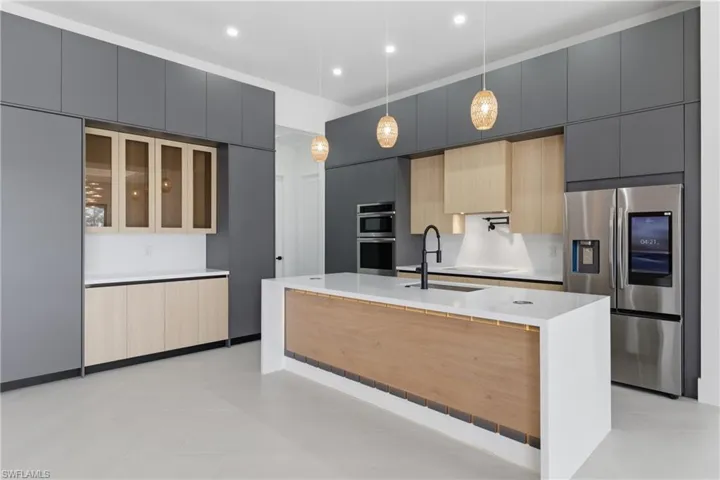 Kitchen with an island with sink, modern cabinets, stainless steel appliances, light stone counters, and two tone color scheme