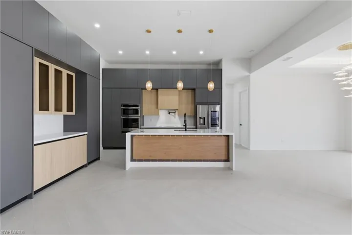 Kitchen with modern cabinets, two tone cabinets, a kitchen island with sink, light stone countertops, and stainless steel appliances