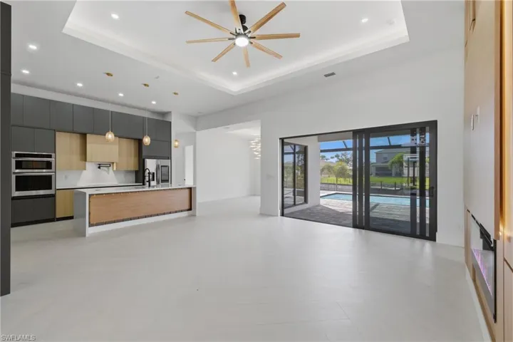 Two tone kitchen with modern cabinets, open floor plan, a ceiling fan, a tray ceiling, and an island with sink