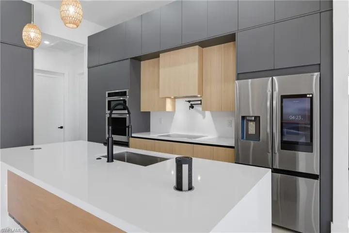Two tone kitchen with modern cabinets, a large island, stainless steel appliances, light stone countertops, and two tone cabinetry